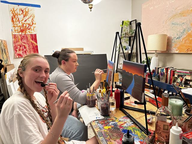 Two guests painting sunset canvases
